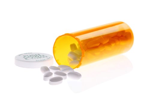 Pills spilling out of a prescription bottle with a safety cap, onto a reflective surface.